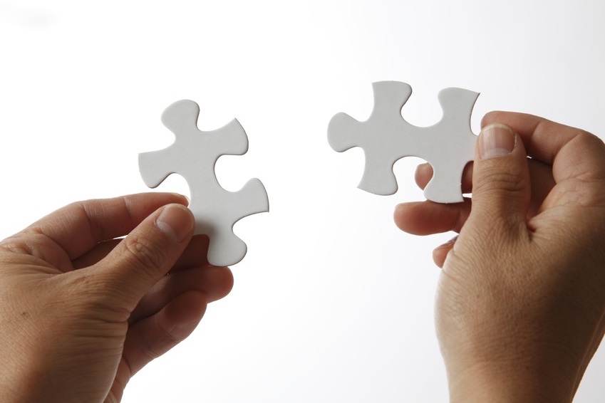 Two hands joining two puzzle pieces as a symbol for tailored compliance solutions